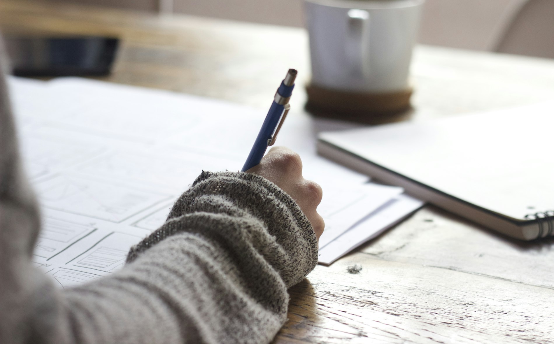 A pair of hands writing notes in an open notebook beside a cup of coffee.