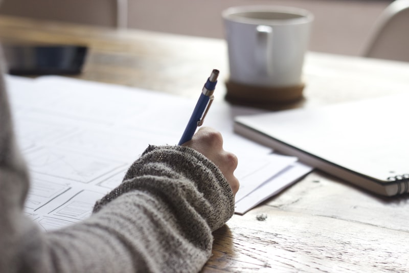 A pair of hands writing notes in an open notebook beside a cup of coffee.