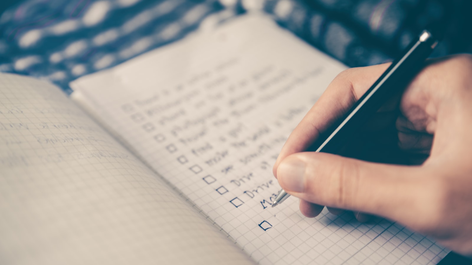 An open planner with a pen resting on a wooden desk near a coffee cup.
