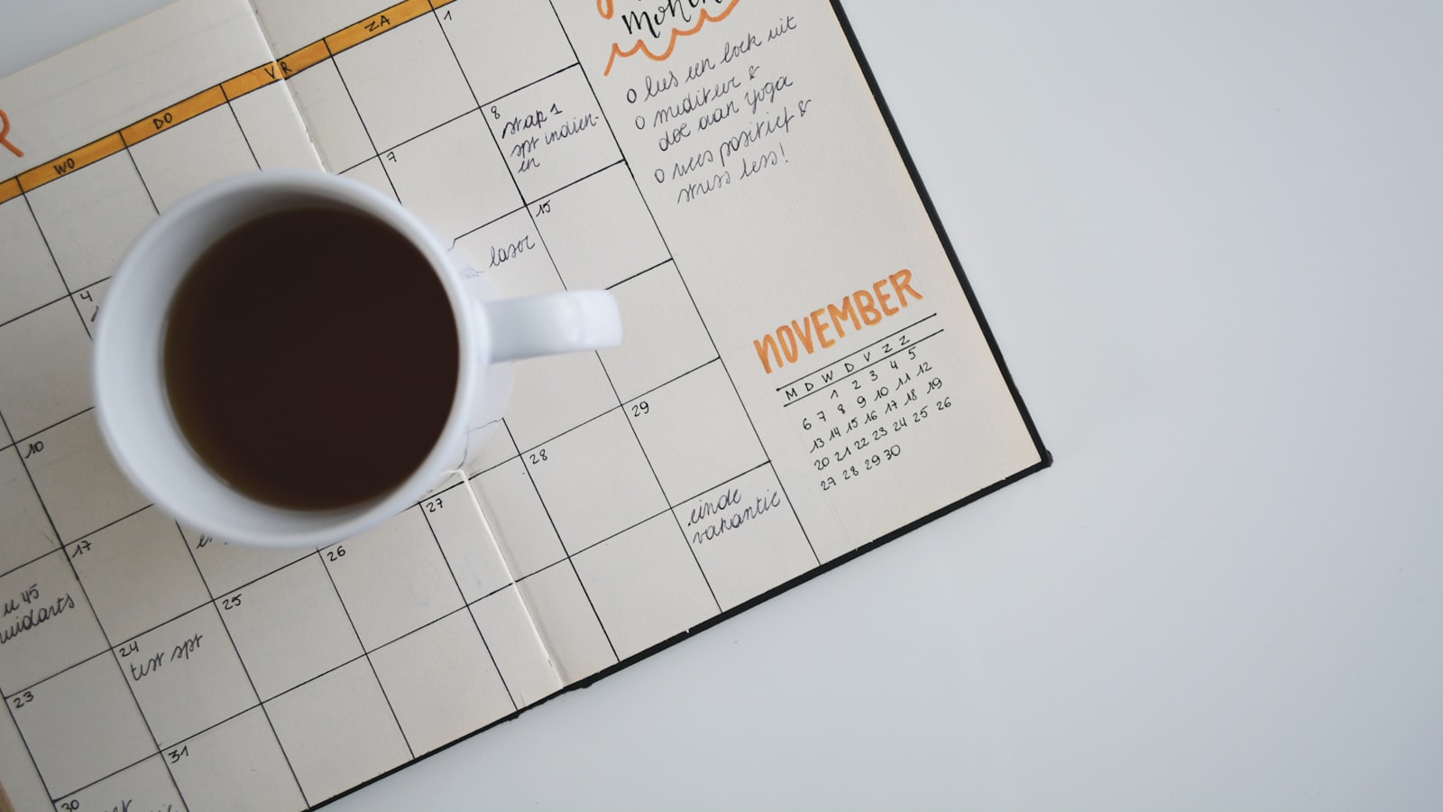 An open paper calendar with dates marked, sitting on a wooden desk.